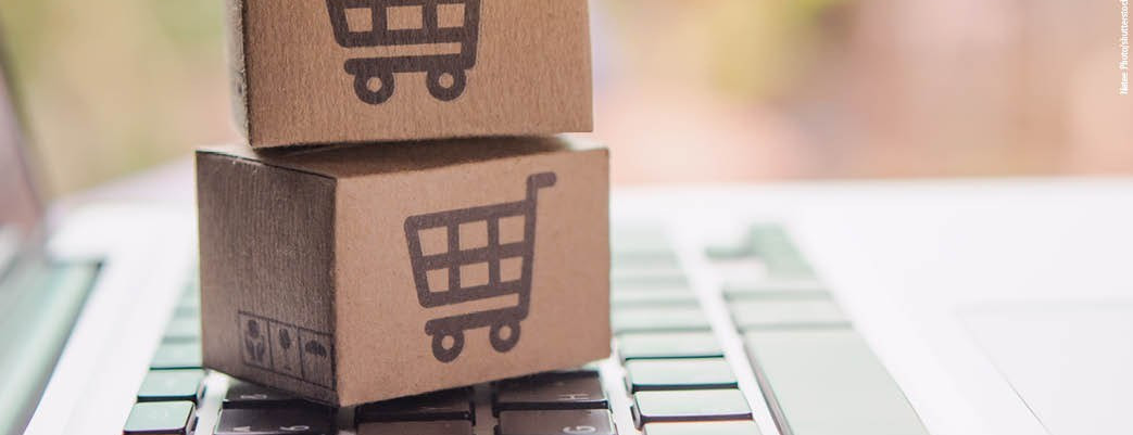Zwei kleine Versandkartons mit Einkaufswagen-Symbol stehen auf einer Computertastatur – Symbolbild für Onlinehandel.