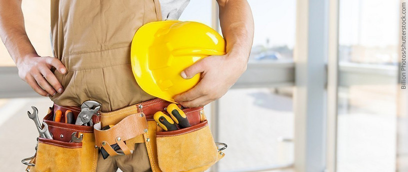 Handwerker mit gelbem Schutzhelm und Werkzeuggürtel, bereit für den Einsatz auf der Baustelle.