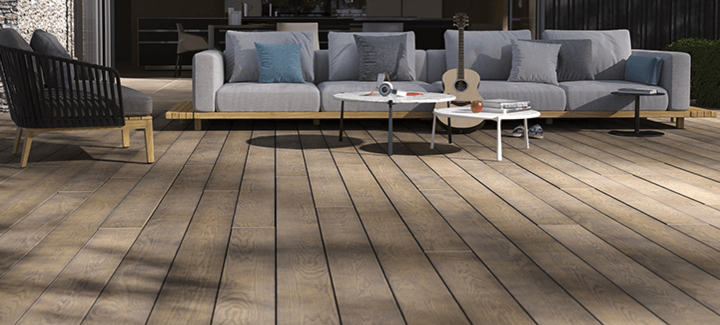 Moderne Terrasse mit edlen Millboard-Dielen in Holzoptik und stilvollen Loungemöbeln – gemütliche Atmosphäre mit Sofa, Tischen und Gitarre.