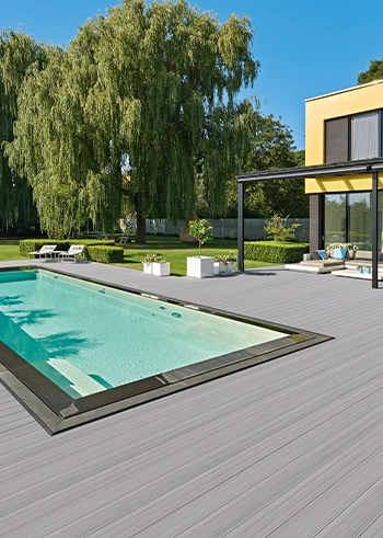 Moderne WPC-Terrasse in Grau mit Pool und stilvoller Gartengestaltung an einem sonnigen Tag.